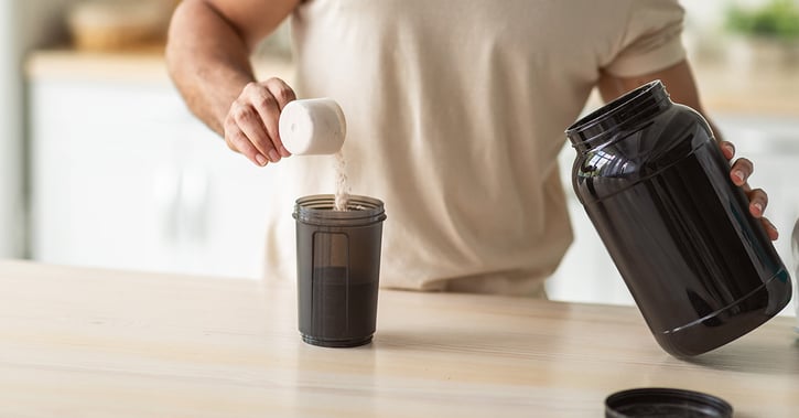 Hand scoops soluble pea protein powder from container into glass