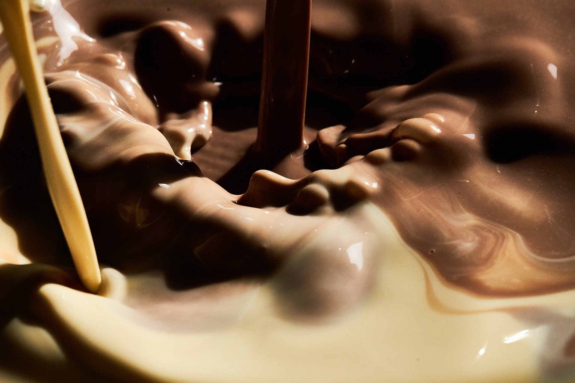 Rich melted chocolate being poured into a bowl with a wooden spoon, swirling with cream in a close-up shot