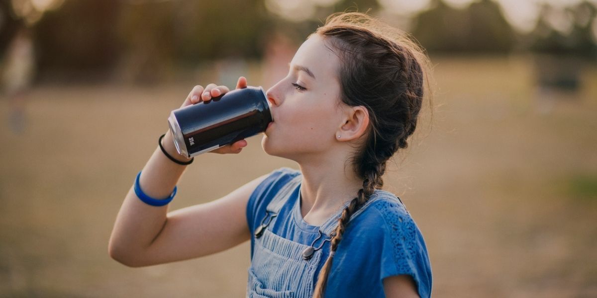 Young girl drinks from soda can while standing outside.